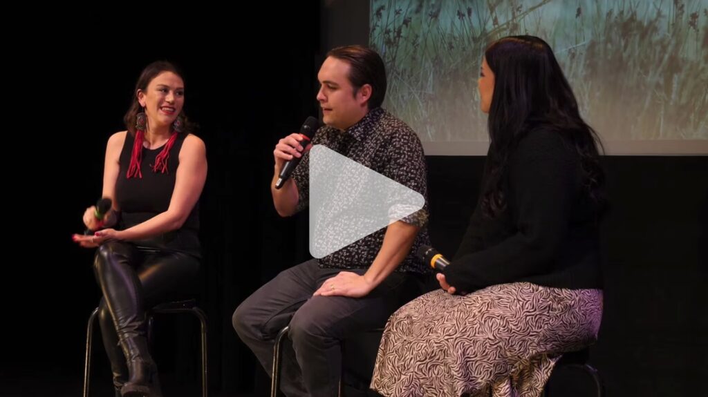 Two women and a man sit on stools in front of a film screen having a conversation while holding microphones