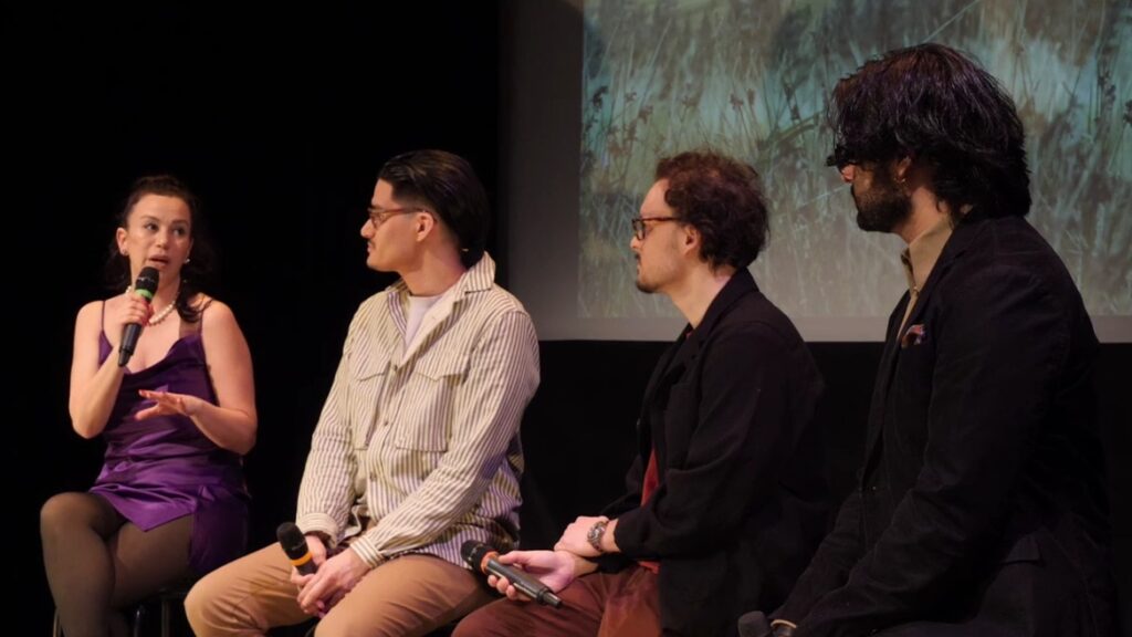 A woman and three men sit on stools holding microphones in front of a film screen