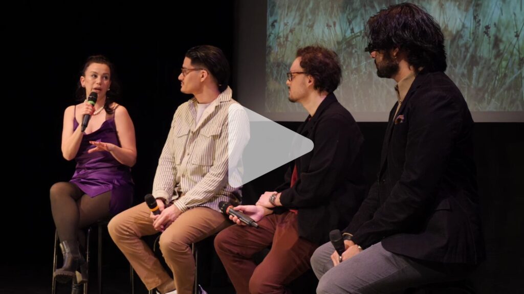 A woman and three men sit on stools holding microphones in front of a film screen