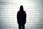 The sillouette of a person wearing a hoodie is in front of a bright white projection screen. Overlapping and blurry words on the screen indicate a website's disclaimer policy.